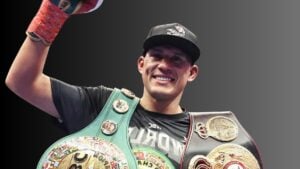 David Benavidez smiling with his fist raised while wearing the WBC light heavyweight title and another championship belt