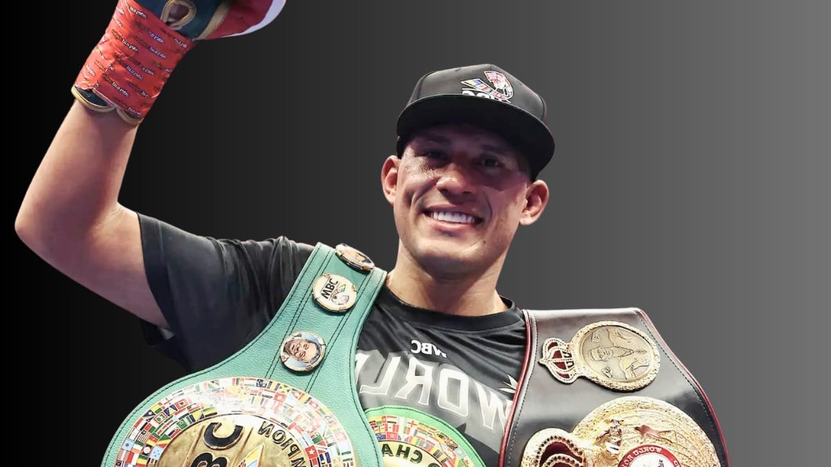 David Benavidez smiling with his fist raised while wearing the WBC light heavyweight title and another championship belt